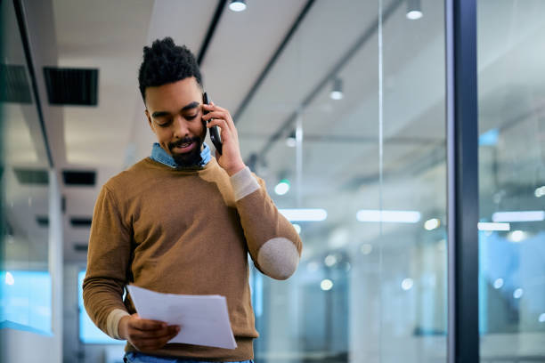 istock Black businessman going through documents while communicating on cell phone in the office. 1483244167