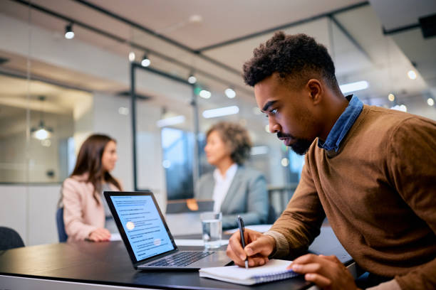 istock Black male entrepreneur using laptop while writing notes during business meeting in the office. 1483244258