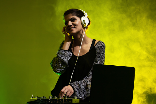 Girl DJ playing music on a mixer. Yellow and green smoke in the background
