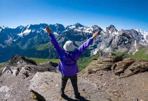 Senior Korean woman at the top of Schilthorn with arms extended, looking at the majestic view of the Swiss Alps in the Jungfrau region, high above Lauterbrunnen and Murren