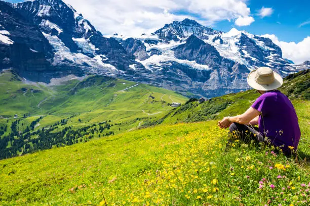 Senior Asian woman enjoying the views of the Swiss Alps from a wildflower covered hilltop on Mannlichen, Switzerland.