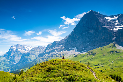 Female hiker sitting on small hilltop on Mannlichen, enjoying the views of the Swiss Alps in the Jungfrau region