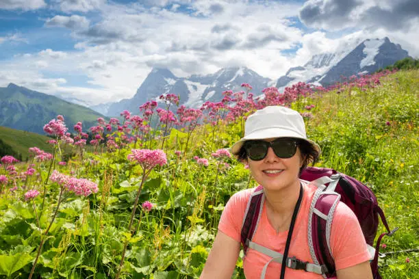 Mature Asian woman hiking the Mountain view trail hike from Murren and leads over the Swiss Alpine meadows and through pine forests from Allmendbhubel to Grutschlap with fantastic views of Eiger, Monch and Jungfrau peaks.