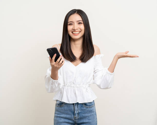 istock Pretty young asian woman using smartphone standing on isolated white background. Excited Beautiful young asian shopping online payment with mobile phone. Playing game on smartphone 1483257391