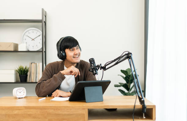giovane asiatico host streaming podcast con microfono a condensatore lavoro su tablet in piccolo studio domestico di trasmissione. creatore di contenuti blogger che registra la voce alla radio intervista conversazione ospite - voice over foto e immagini stock