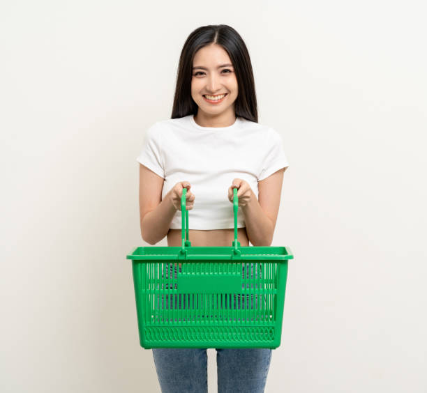 Happy beautiful woman holding shopping basket. Portrait beautiful asian female in fashion style standing pose on isolated background. Young asian woman shopping at online market application Happy beautiful woman holding shopping basket. Portrait beautiful asian female in fashion style standing pose on isolated background. Young asian woman shopping at online market application holding shopping basket stock pictures, royalty-free photos & images