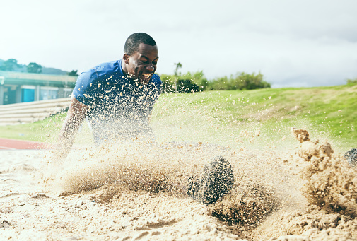 Long jump, fitness and black man in the sand for sports, exercise and competition in the USA. Energy, speed and African athlete training for a sport challenge, jumping and landing with power