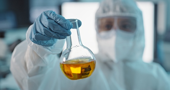 Hand of scientist with hazmat suit, liquid solution in glass and test for biohazard, virus or pharmaceutical research. Science, danger and vaccine development, woman in protective gear in laboratory.