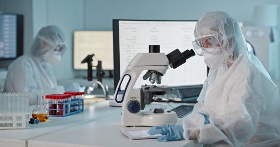 Microscope, medical research and protection gear in a laboratory with scientist worker doing work. Virus expert, working and safety in science lab with biohazard suit and staff with mask from risk