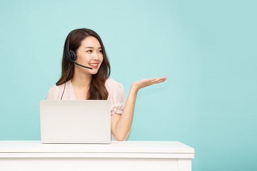 Young Asian businesswoman call center with headsets sitting and using laptop computer isolated over green background, Telemarketing sales or Customer service operators concept
