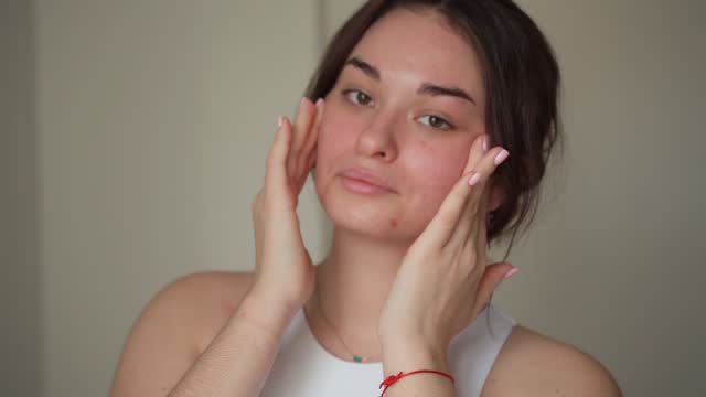Young woman pplying moisturizing cream to face worried caused of acne inflammation and acne scar occur on her face. Teenage girl Inflamed acne consists of swelling, redness, and pores that are deeply clogged with bacteria, oil, and dead skin.