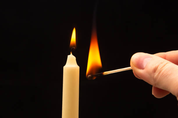 istock Lighting a candle with a wooden match on a dark background. Burning candle fire 1483268370