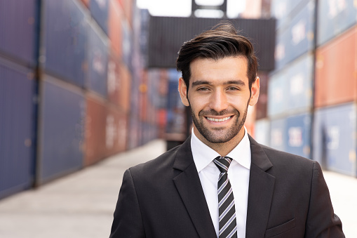 Happy business man wearing a suit and tie is standing in a shipping yard with a smile on his face