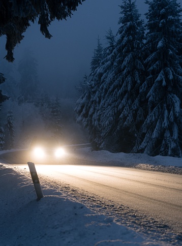 A vertical of car's headlights illuminating a snow-covered road in a forest at night