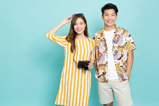 Asian couple ready for vacation poses holding a camera and wearing sunglasses isolated on green background