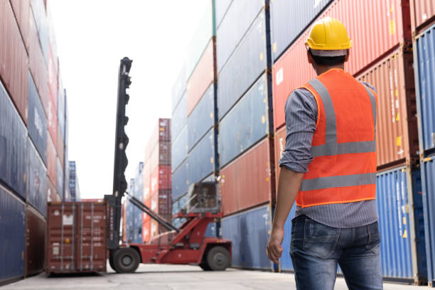 istock A worker at a shipping yard standing and looking at forklift helps it move a red container during his work day in container warehouse 1483271189
