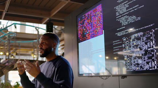 Close up stock photograph of a black man conducting a seminar on Python computer coding in an open plan work arena.