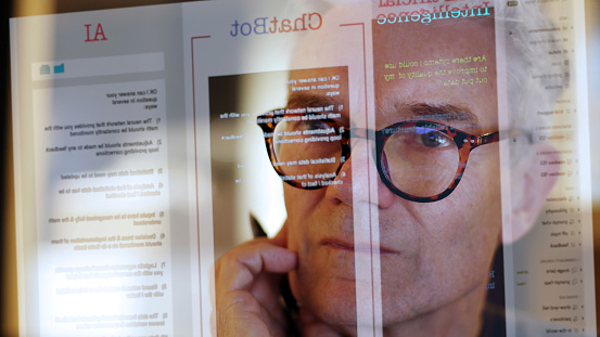 Close up stock photograph of a mature man studying a see-through computer monitor that’s displaying text provided by an AI (artificial intelligence) chatbot.