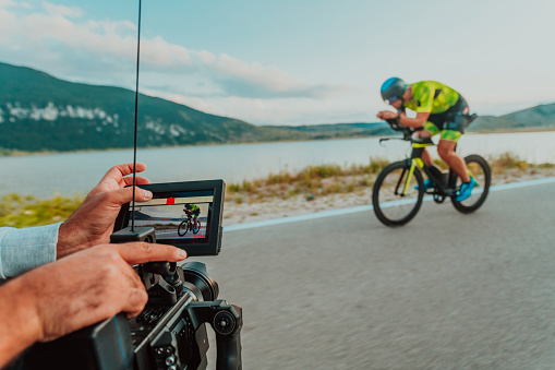 A cameraman with professional equipment and camera stabilization films a triathlete on the move riding a bicycle.