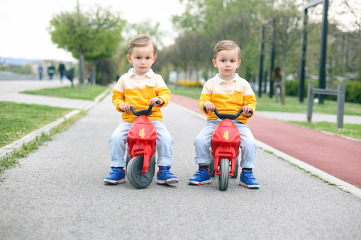 Two twin brothers driving toy motorcycles. About 3 years old, Caucasian male boys.