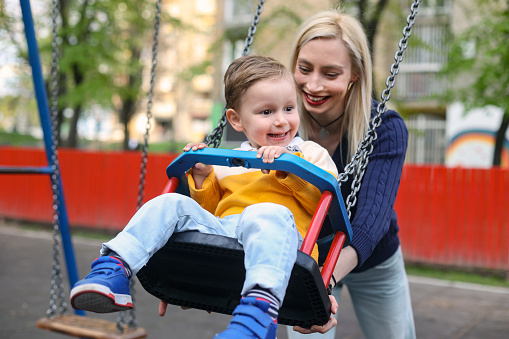 Boy and his mother having fun on a swing. About 3 years old, Caucasian male boy.