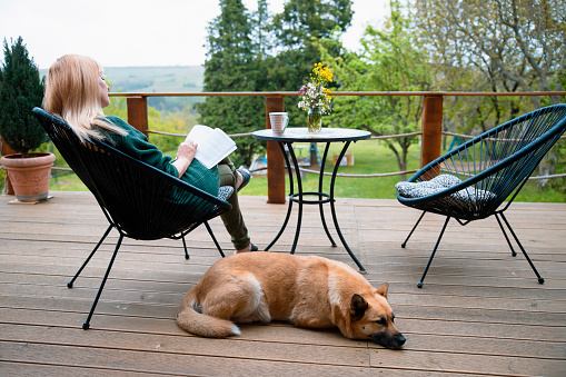 Woman reading book on the porch, resting with her dog