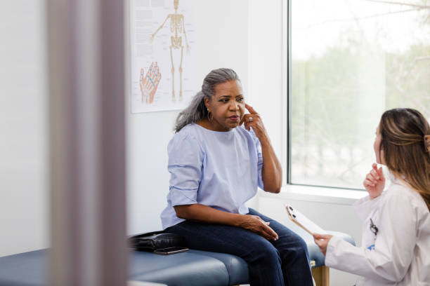Female patient points to ear while discussing symptoms with doctor stock photo