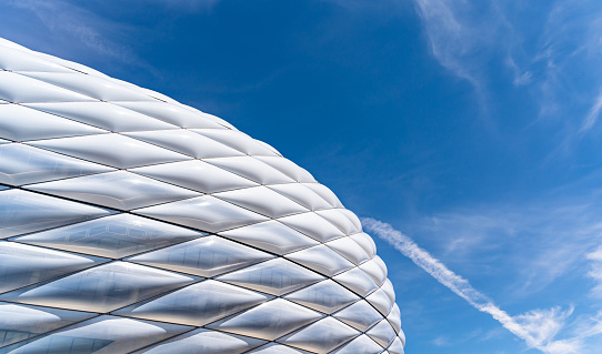 This stock photo captures the majestic Allianz Arena in Munich, Germany, on a sunny day with no fans in the stadium. The sun rays shine down on the empty green field, creating a calm and peaceful atmosphere.

The curved lines and white lattice pattern on the exterior of the stadium are particularly visible in this image, giving the stadium a modern and futuristic appearance.

Without fans in the stadium, one can better appreciate the size and grandeur of the stadium. The empty arena creates a sense of stillness and emptiness that invites the viewer to focus on the architecture of the stadium.

Overall, this image exudes a calming atmosphere that captures the majestic look of the Allianz Arena on a sunny day.