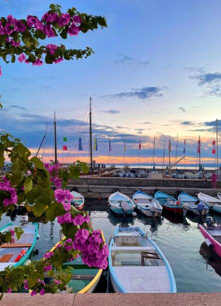 ガルダ湖に沈むロマンチックな夕日と、停泊中のボートと花がシーンを完成させます。 - lake garda sunset blue nautical vessel ストックフォトと画像