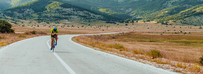 Full length portrait of an active triathlete in sportswear and with a protective helmet riding a bicycle. Selective focus.