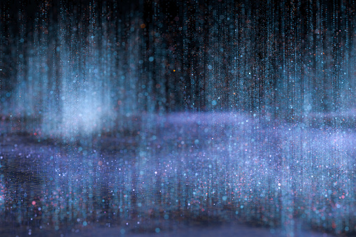 Lots of blue drops, dots and particle fall vertically on a dark background. Abstract background, three dimensional digitally generated picture, vanishing and diminishing perspective of objects of image, field blur effect