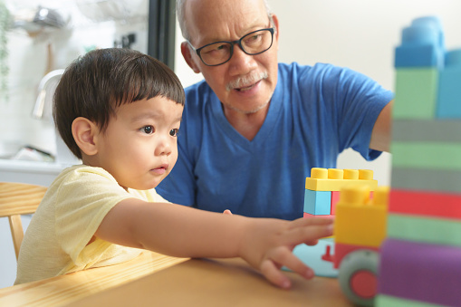 Asian Grandson and his Grandfather playing colorful plastic toy blocks at home. Chinese child boy with Senior man.