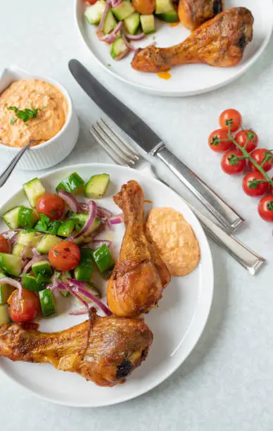 Delicious summer meal with baked or grilled chicken drumsticks. Served with a delicious paprika, feta cheese dip and marinated zucchini, cherry tomato salad. Served on plates on white table background from above.