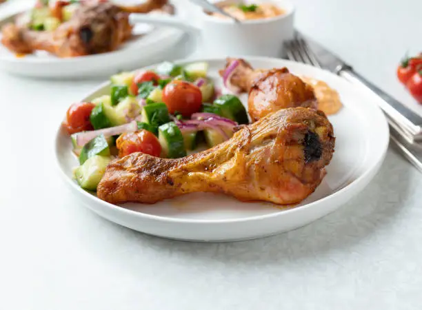Delicious light low carb dinner or lunch with oven baked chicken drumsticks and a marinated zucchini, roasted tomato salad. Served with a fresh paprika, feta cheese dip on a plate on white background. Closeup and front view with copy space.
