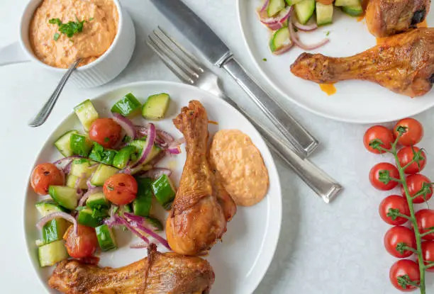 Delicious low carb chicken dish with a fresh cherry tomato, zucchini salad and paprika feta cheese dip. Served ready to eat on plates on white background from above.