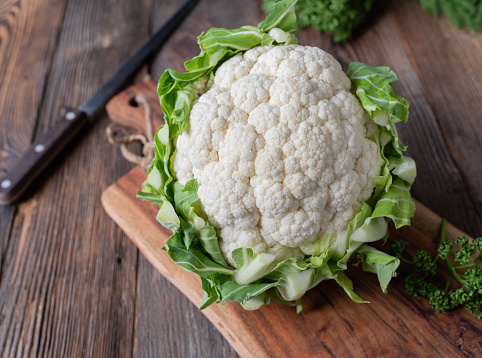 Raw and uncooked whole cauliflower head with green leaves isolated on a wooden cutting board with knife. Closeup with copy space