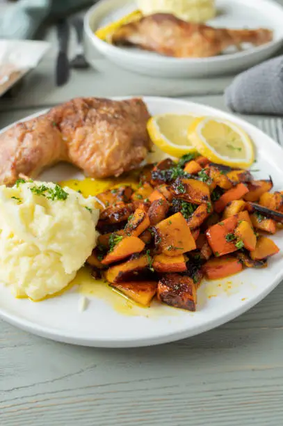 Delicious healthy and gluten free dinner with oven baked chicken legs, mashed potatoes and a delicious warm pumpkin salad. Served ready to eat on a plate on kitchen table background. Closeup, front view with copy space