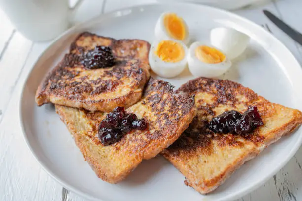 Delicious breakfast with whole grain french toast and blueberry jam. Served with boiled eggs on a plate