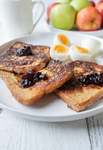 Delicious homemade breakfast plate with fresh pan fried french toast. Topped with blueberry jam and served with boiled halved eggs. Closeup, front view
