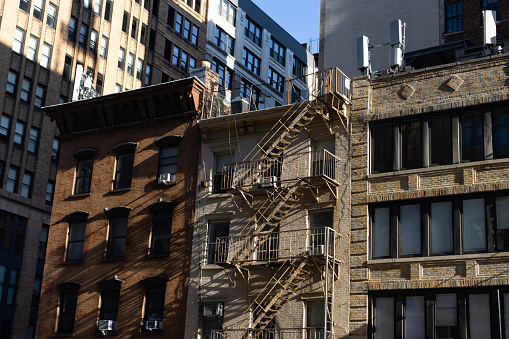 A row of small old brick buildings with fire escapes along a street in Chelsea of New York City