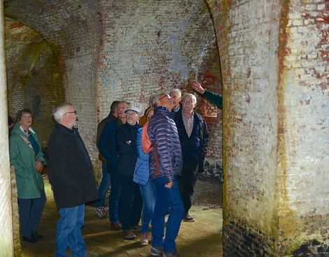 Schaffen, Vlaams-Brabant, Belgium - April, 17, 2023: older visitors listen to the guide with the green arm explaining the features and history of a very old curved circular building with white painted walls