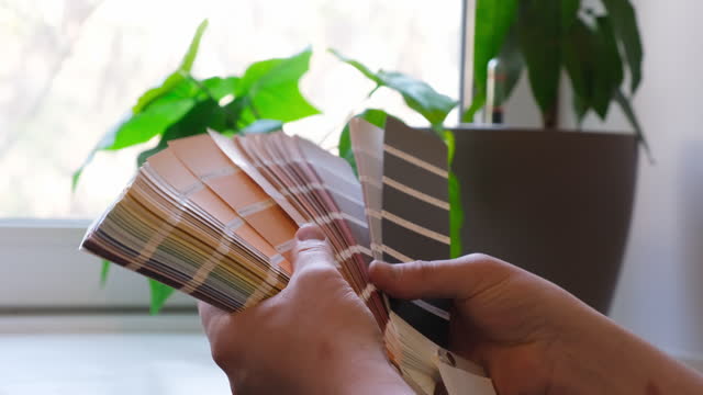 The designer holds pantone fan of color guide in hand. Selection of colors for the color of the walls apartment distribution during promotion concept
