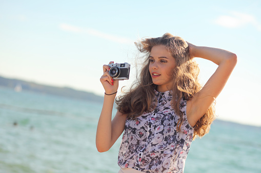 Young woman at the sea taking photos with vintage camera.