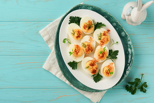 Stuffed or deviled eggs with paprika and parsley on blue plate for easter table. Traditional dish for Easter. Healthy diet food for breakfast. Top view, flat lay.