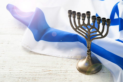 Happy Hanukkah. Hanukkah old Menorah against background of the Israeli flag with sunlight or bokeh on white wooden background. Religion image of jewish holiday Hanukkah background.