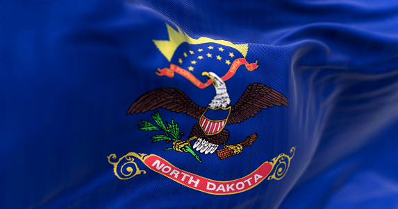 Close-up of North Dakota state flag waving. Blue with coat of arms. Eagle above “North Dakota” scroll. 3d illustration render. Textured background. Selective focus. Fluttering textile
