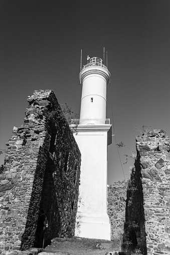 An aerial grayscale shot of a lighthouse on a cliff overlooking an island