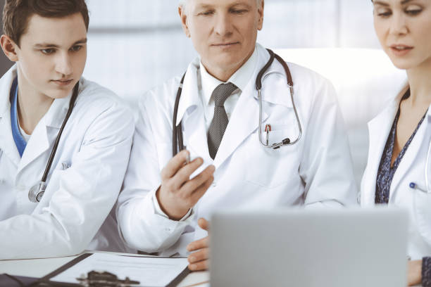 istock Doctors colleagues and elderly therapist discussing current disease therapy while sitting at working place in sunny clinic. Teamwork in medicine 1483311077