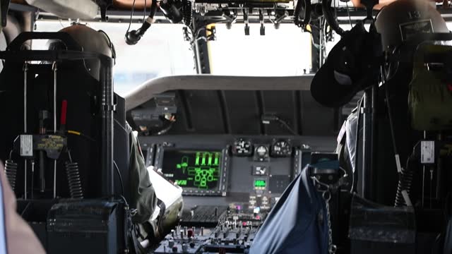A pilot in a cockpit holds a joystick to control a helicopte