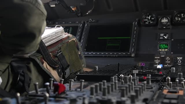 A pilot in a cockpit holds a joystick to control a helicopte